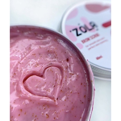 Creme rosa esfoliante com partículas marrons em pote aberto e tampa com texto ao fundo.