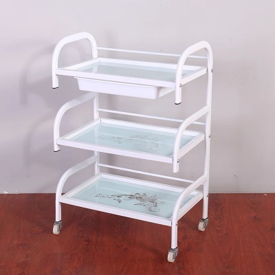 Carrinho móvel branco de metal com três prateleiras de vidro decoradas com flores