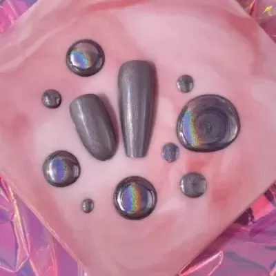 Unhas postiças e gotas de verniz holográfico cinza em superfície rosa marmoreada