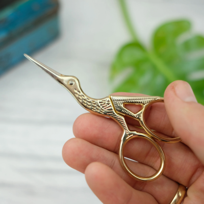 Tesoura dourada em forma de pássaro segurada por uma mão com anel dourado