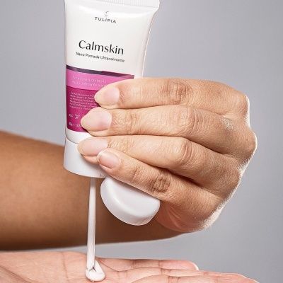 Pessoa a aplicar creme Calmskin da TULIPIA na palma da mão com bisnaga branca e texto visível.