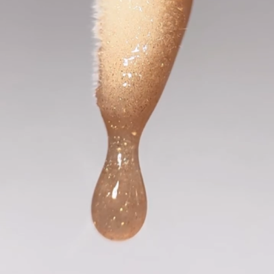 Textura viscosa translúcida com partículas douradas formando gota