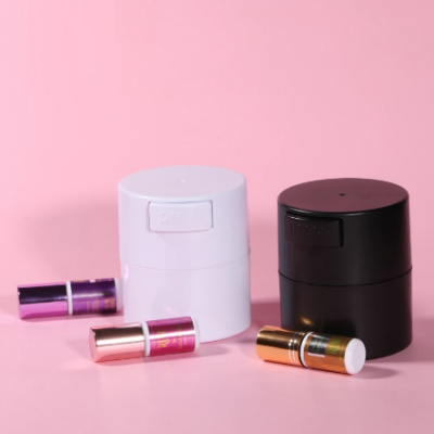 Dois recipientes cilíndricos branco e preto e três sticks de batom coloridos sobre fundo rosa.