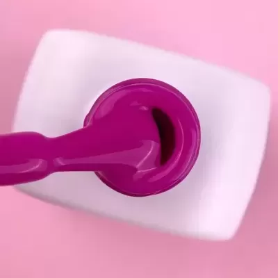 Pincel de verniz de unhas cor rosa fúcsia num frasco aberto sobre superfície branca