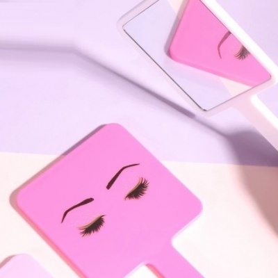 Espelho de mão cor de rosa com ilustração de sobrancelhas e pestanas em preto