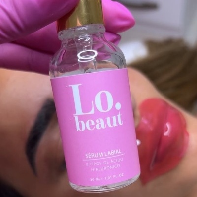Frasco de sérum labial Lo. beaut com rótulo rosa e tampa dourada segurado por mão com luva rosa