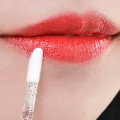 Lábios vermelhos com gloss aplicado por aplicador transparente com partículas