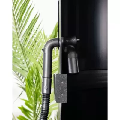 Aspirador de pó vertical preto com mangueira flexível e planta verde ao fundo
