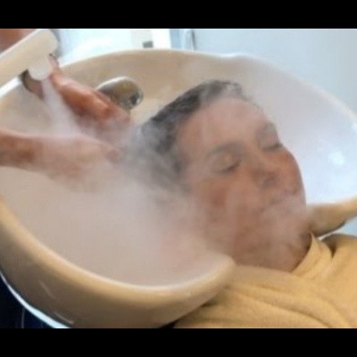 Pessoa a receber lavagem de cabelo com vapor numa bacia branca de cabeleireiro