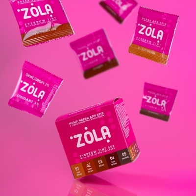 Conjunto para tintura de sobrancelhas ZOLA em embalagem e saquetas cor-de-rosa sobre fundo rosa
