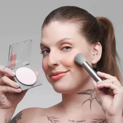 Mulher a aplicar pó compacto com pincel em fundo cinzento