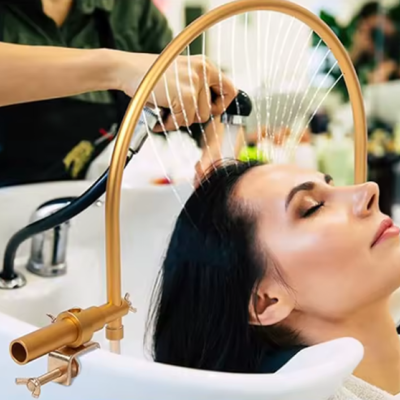 Mulher a lavar cabelo numa pia com pulverizador e estrutura dourada