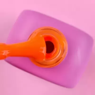 Verniz laranja com pincel e tampa roxa, fundo rosa