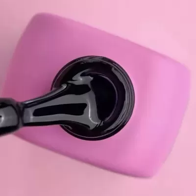 Frasco aberto de verniz preto com pincel, sobre objeto rosa