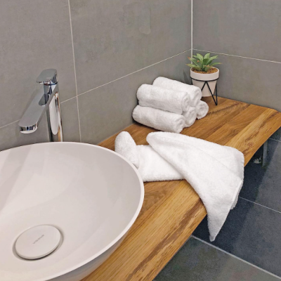 Lavatório branco redondo com torneira metálica e toalhas brancas numa bancada de madeira