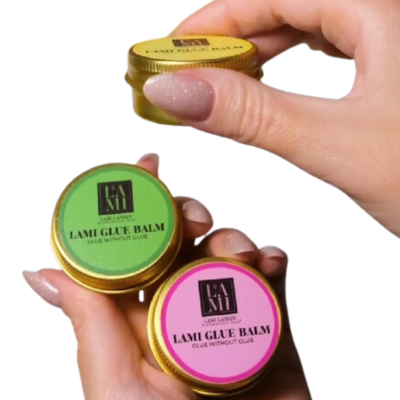 Três frascos dourados de LAMI GLUE BALM com rótulos verde e rosa, segurados por mãos com unhas pintadas