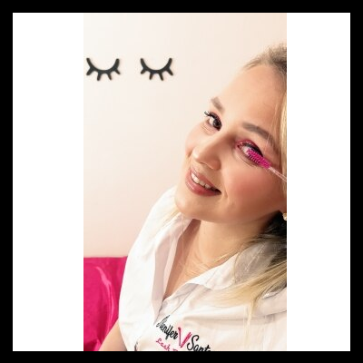 Mulher a aplicar máscara de pestanas rosa com camisa branca e adesivos de olhos na parede branca.