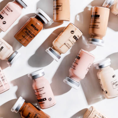 Frascos de vidro com bases de maquilhagem em vários tons sobre fundo branco