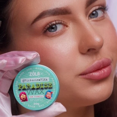 Frasco verde de cera para cabelo segurado por mulher com luva rosa