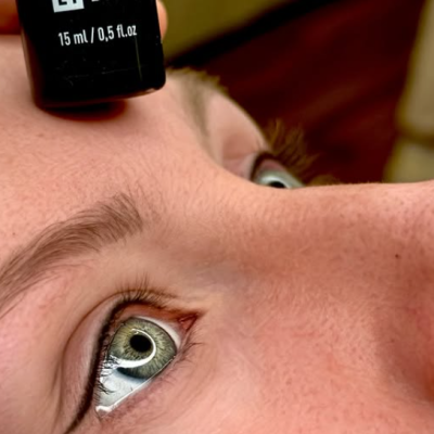 Frasco preto de esmalte E1 Devil perto do rosto de uma pessoa com olhos verdes