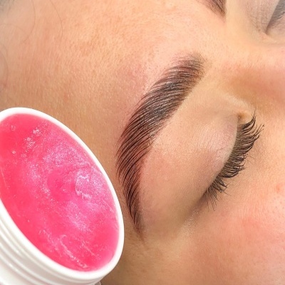 Rosto com sobrancelha definida e conteúdo rosa num recipiente branco aberto