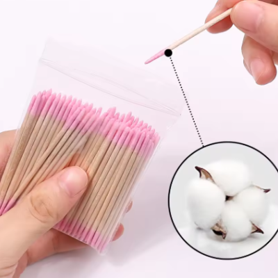 Cotonetes de madeira com pontas cor-de-rosa num saco transparente e detalhe de algodão