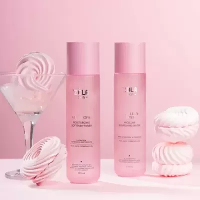 Produtos de cuidados de pele ZOLA SKIN em garrafas cor-de-rosa com suspiros cor-de-rosa e copo de cocktail sobre fundo cor-de-rosa.