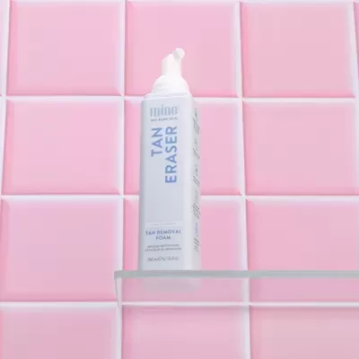 Frasco de espuma TAN ERASER branco e azul em prateleira de vidro com azulejos cor-de-rosa