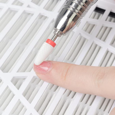 Broca de cerâmica branca com base vermelha numa máquina elétrica para manicure sobre unha com verniz rosa cintilante