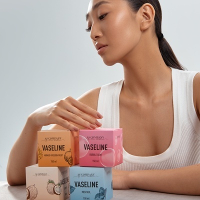 Caixas coloridas de vaselina AS COMPANY com sabores diferentes e mulher atrás