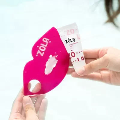 Tubo branco de creme ZOLA e espátula rosa em formato de lábios com creme