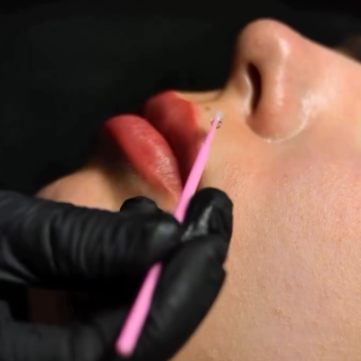 Aplicação de produto na pele com ferramenta cor-de-rosa perto dos lábios vermelhos