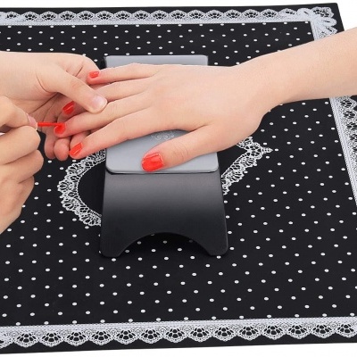 Mãos a pintar unhas com verniz vermelho sobre almofada cinza e pano preto com bolinhas brancas e renda.