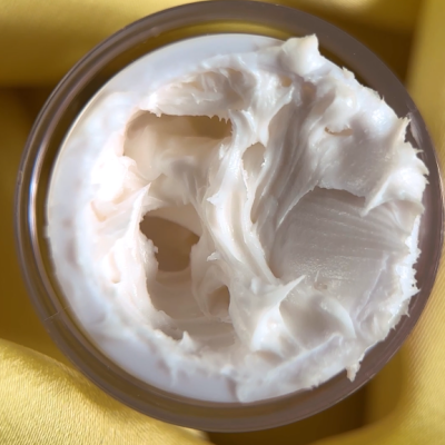 Frasco aberto com creme branco sobre tecido amarelo