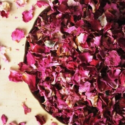 Tigela de madeira com pétalas secas de rosa vermelhas e rosas sobre superfície de madeira clara