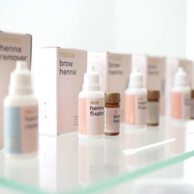 Produtos de henna para sobrancelhas Nossa em frascos e embalagens brancas com detalhes rosas e bege sobre vidro