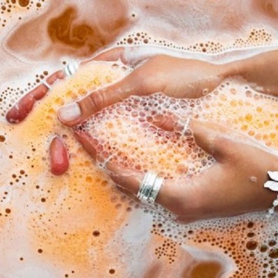 Mãos com anéis em água espumosa laranja e bege