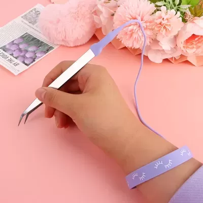 Pinça com pulseira antiestática lilás em mão sobre fundo rosa com flores.