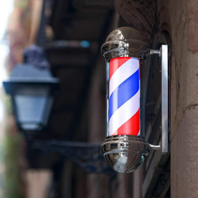 Cilindro de barbeiro clássico com luzes vermelha, branca e azul montado numa parede de pedra