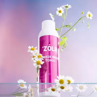 Frasco branco com rótulo rosa de tónico com flores ao redor e fundo lilás.