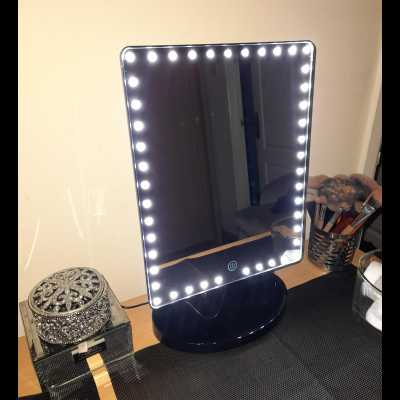 Espelho de maquilhagem LED com base preta sobre mesa com pincéis e estojo decorativo