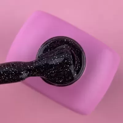 Close-up de esmalte preto com glitter em escova sobre apoio rosa.