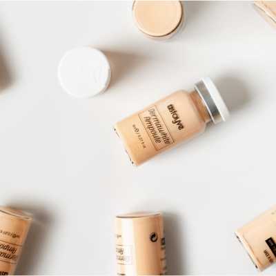 Frascos de base líquida bege claro com tampas metálicas sobre fundo branco