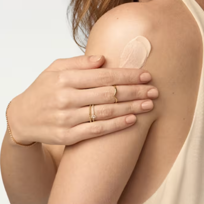 Braço de mulher com creme aplicado e mãos com joias douradas