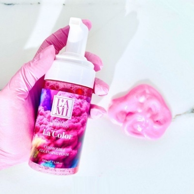 Frasco de espuma de limpeza com rótulo colorido segurado com luva rosa e espuma rosa ao lado