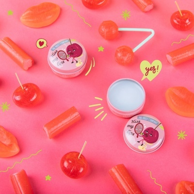 Frascos de bálsamo labial rosa rodeados por doces vermelhos e corais sobre fundo rosa