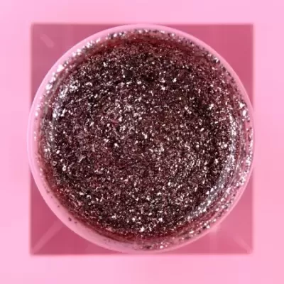 Pote de gel roxo brilhante com partículas prateadas em fundo rosa