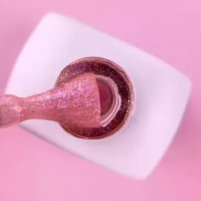 Frasco de verniz com tampa branca e pincel com verniz rosa glitter