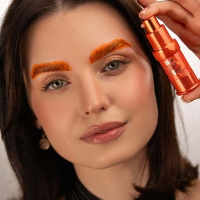 Mulher segurando frasco metálico laranja e com sobrancelhas laranja