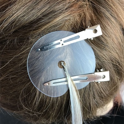 Presilha transparente redonda com grampos metálicos em cabelo castanho e loiro.